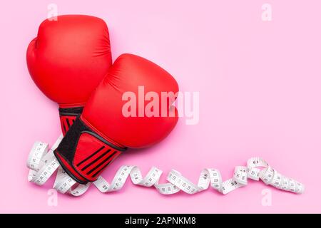 Gesundes Lifestyle- oder Gewichtsverlustkonzept. Boxhandschuhe und Maßband isoliert auf pinkfarbenem Hintergrund. Kopierbereich Stockfoto