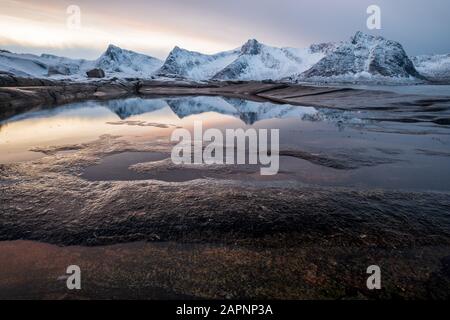 Blick über den Rockpool auf die verschneite Bergkette bei Abendlicht mit schönen Reflexionen, Kap Tungeneset, Ersfjord, Senja, Norwegen Stockfoto