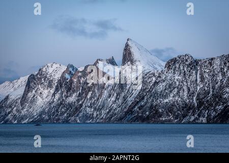 Beeindruckende schneebedeckte Bergkette von Segla über einen Fjord im Winter unter blauem Himmel, Senja, Norwegen Stockfoto