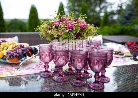 Schönen Gläser von Violett Glas auf dem Tisch mit Beeren und Blumen, Komposition für Catering im Freien Stockfoto