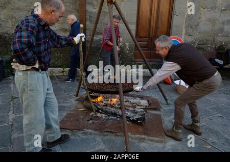 Die Einheimischen braten während des Oktoberfests, das die Kastanienernte feiert, bei einem offenen Feuer im toskanischen Bergdorf Gavinana Kastanien. Stockfoto