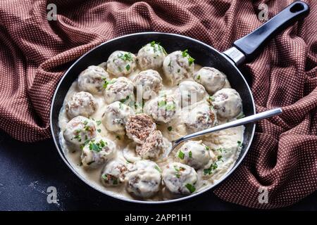 Klassische schwedische Fleischbällchen mit cremiger Sauce und Petersilie in einem Skillet auf einem Küchentisch aus Beton, horizontaler Blick von oben Stockfoto