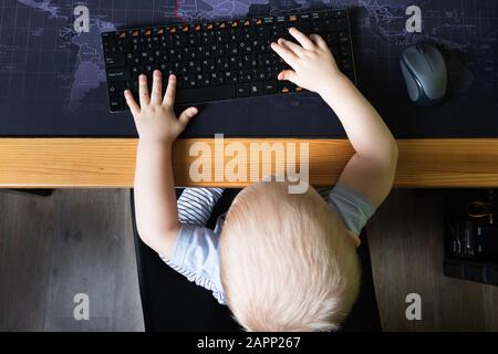 Die Draufsicht des kleinen Jungen sitzt an einem Computer und hält eine Tastatur in den Händen Stockfoto