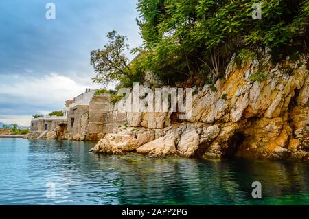 Klippen in der Nähe von Hafen und Sablicevo Strand in Rijeka, Kroatien. Felsige Küste im Osten der Stadt mit kleinen Stränden, Hotels, Gebäuden und Klippen, die mit bedeckt sind Stockfoto