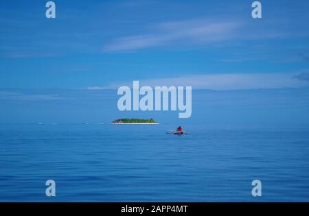 Ein kleines Einzelboot auf dem Meer. Das Meer und der Himmel sind so blau, dass sie miteinander verschmelzen. Ein einsames Schiff fährt auf eine kleine Insel zu. Stockfoto