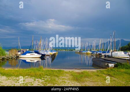 Ein kleiner Hafen an einem Chiemsee (Bayern, Deutschland) an einem ruhigen, schönen und sonnigen Sommertag. Mehrere Segelboote sind auf zwei Piers abgestellt. Stockfoto