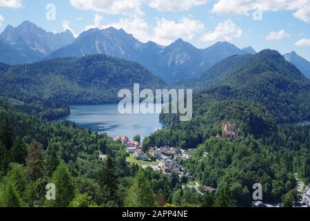 Ein Blick auf das Tal mit dem blutigsten See, dem kleinen Dorf und dem Wahrzeichen der Burg Hohenschwangau. Das Wasser ist von bewaldeten Bergen umgeben. Stockfoto