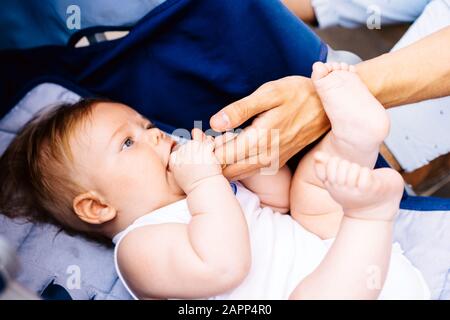 Neugeborenes Baby, das in einem blauen Kinderwagen liegt, greift mit seinen Armen die Hand seines Vaters Stockfoto