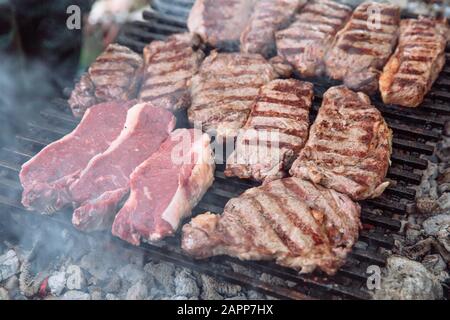 Der Prozess des Kochens Stück Steak auf dem Grill. Stücke von Gegrilltem und rohes Fleisch. Stockfoto