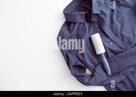 Dunkelfarbiges Hemd mit statischem Ankleben, bedeckt mit Staub, Fusseln, Flusen und Haaren und klebriger Rolle zum Reinigen der Kleidung. Isoliert auf Weiß mit Copyspace Stockfoto