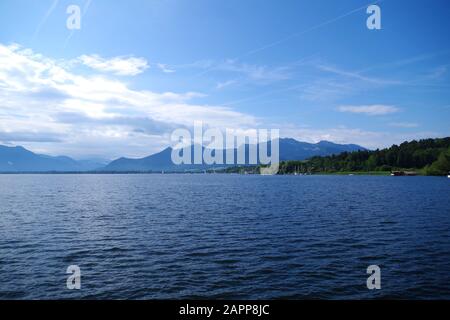 Blick auf die ruhigen Gewässer des Chiemsee (Bayern, Deutschland). In der Ferne befinden sich Berge und bewaldete Inseln. Der Himmel ist sehr blau. Stockfoto