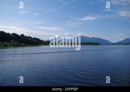 Blick auf die ruhigen Gewässer des Chiemsee (Bayern, Deutschland). In der Ferne befinden sich Berge und bewaldete Inseln. Der Himmel ist sehr blau. Stockfoto