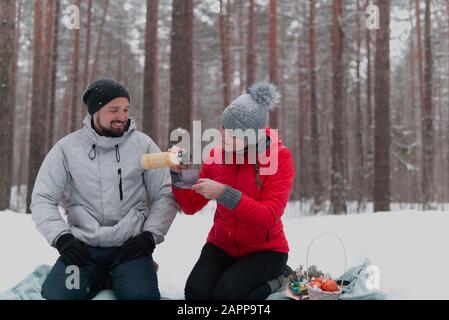 Junge Paare haben Picknick im winterlichen verschneiten Wald, Frau gießt Tee Stockfoto