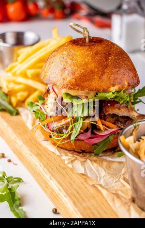 Vegetarischer Frischburger mit Pilzen und Gemüse, serviert mit pommes frites auf einem Holzbrett, gesundes Fast-Food, Closeup Stockfoto