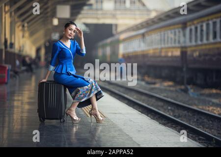 Reisende Frau im Bahnhof wartet auf Reisen. Junge Geschäftsfrau lächelnd sitzend mit Reisekofferwagen, in Wartehalle de Stockfoto