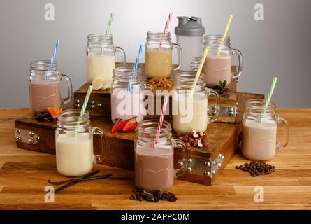 Verschiedene Arten von farbenfrohen Milchshake in Mason Gläsern mit Papierstraten und Zutaten auf einer Holztischplatte Stockfoto