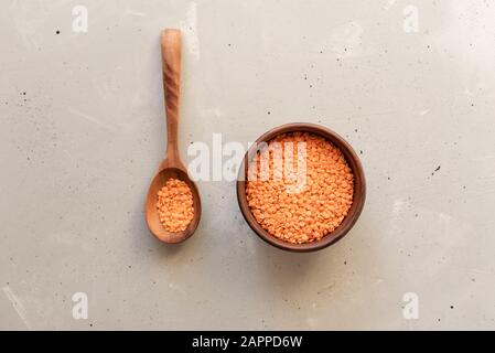 Rote Linsen in Holzplatte auf grauem Hintergrund. Stockfoto