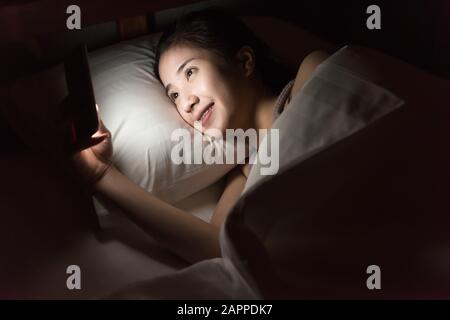Frau, die Nutzung von Mobiltelefonen und liegend auf Bett Stockfoto