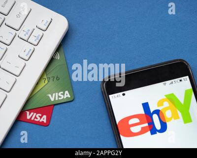 Computertastatur, zwei Visa-Bankkarten und ein Smartphone mit eBay-Logo auf blauem Hintergrund Stockfoto