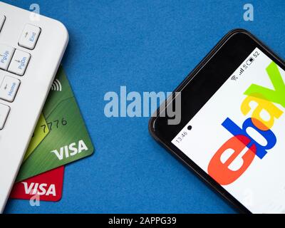 Computertastatur, zwei Visa-Bankkarten und ein Smartphone mit eBay-Logo auf blauem Hintergrund Stockfoto