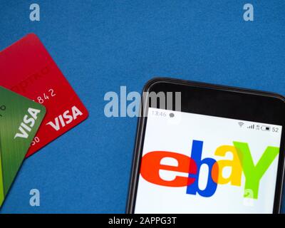 Zwei Visa-Bankkarten und ein Smartphone mit eBay-Logo auf blauem Hintergrund Stockfoto