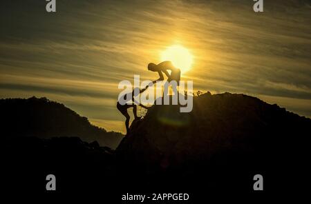 Silhouette der helfenden Hand zwischen zwei Jungen klettern Stockfoto