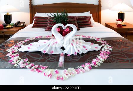 Romantisches Schlafzimmer Innenraum, Küssen Swan Origami Handtücher und streute frische Rosa Weiße Rose Blumenblätter Dekoration auf dem Bett für frisch verheiratete Paare. Weddin Stockfoto