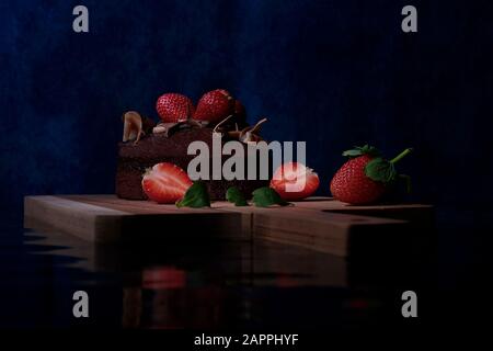 Schokoladenkuchen mit Erdbeeren auf einem Holzbrett mit einer Spiegelung der Welligkeit des Wassereffekts Stockfoto