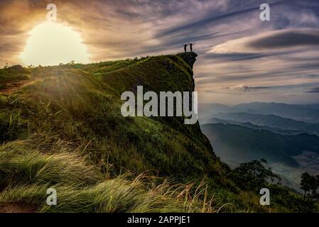 Junge Frau, die auf dem Rand der Klippe steht und mit erhobenen Händen auf einen Himmel blickt, Sunrise Szene mit dem Gipfel der Berg- und Wolkenlandschaft bei Phu Chi fa in C Stockfoto