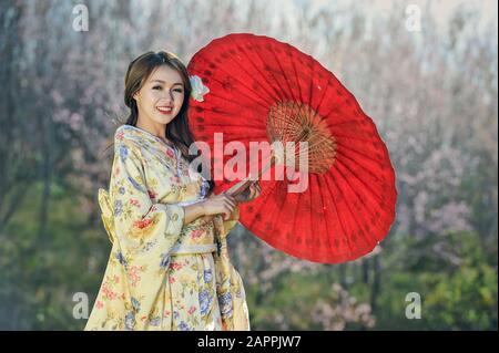 Attraktive asiatische Frau mit traditionellem japanischen Kimono mit rotem Regenschirm Stockfoto
