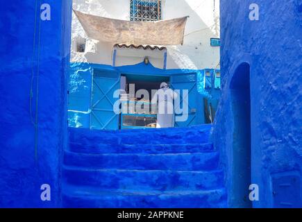 Mann in typisch marokkanischer Kleidung, der eine Straße in der Stadt Chefchaouen unterläuft. Stockfoto