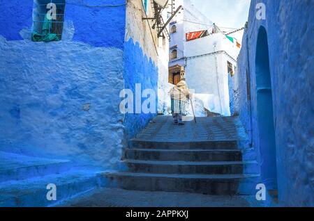 Frau in typisch marokkanischer Kleidung, die in der Stadt Chefchaouen eine Straße hinunterläuft. Stockfoto