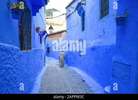 Mann in typisch marokkanischer Kleidung, der eine Straße in der Stadt Chefchaouen unterläuft. Stockfoto