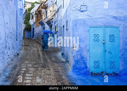 Frau in typisch marokkanischer Kleidung, die in der Stadt Chefchaouen eine Straße hinunterläuft. Stockfoto