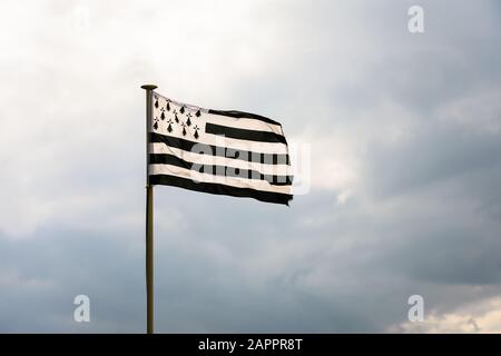 Flagge der Bretagne mit dem Namen Gwenn ha Du auf bretonisch, die im Wind an vollem Mast gegen einen stürmischen Himmel fliegt. Stockfoto