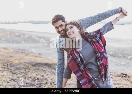 Fröhliches junges fröhliches Paar, das in der Herbstsaison lustige Momente am Strand miteinander lachen und Text finden kann Stockfoto