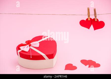 Herzförmige Geschenkbox und rote Papierherzen auf pinkfarbenem Pastellhintergrund. Kleider Haken und rotes Papier Herzen auf Seil. Valentines Tageskonzept Stockfoto