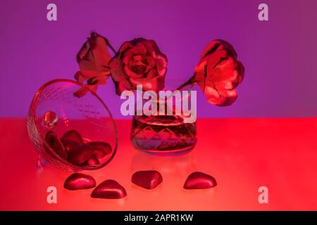 Stillleben von Blumen in Vase und herzförmigen Pralinen, rot und violett. Valentinstag Stockfoto