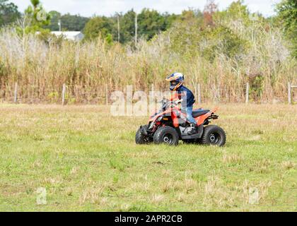 Kinder, die ein 4-Rad im Land fahren. Der Fahrer trägt einen Helm. Das Kind ist 6 Jahre alt. Stockfoto