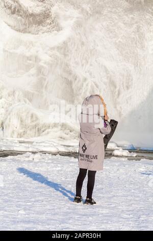 Besucher trägt die Art und Weise wir Leben Glück & Erfolg Mantel am Skogafoss Wasserfall, Island im Januar mit gefrorenen Eiszapfen Stockfoto