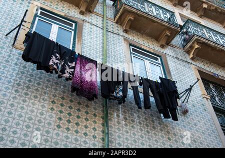 Hauswäsche mit farbenfroher Kleidung, die an einem Seil vor einem Haus zum Trocknen hängt. Stockfoto