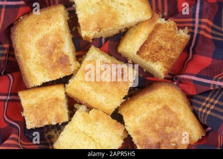 Hausgemachtes gelbes Maisbrot mit knuspriger Kruste in Scheiben geschnitten und auf einem sauberen, neuen, rot-blau gefärbten Küchentuch mit kariertem Muster serviert. Stockfoto