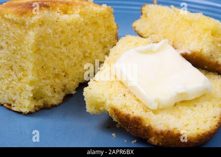 In Scheiben geschnittenes, hausgemachtes gelbes Speisebrot mit einem Klaps echter Butter, die auf das heiße Brot schmilzt. Serviert auf einer blauen Keramikplatte. Stockfoto