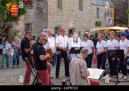 Locronan Dorfplatz; eine Gruppe traditioneller keltischer Sänger versammelt sich am Abend am Dorfplatz und singt traditionelle Volkslieder Stockfoto