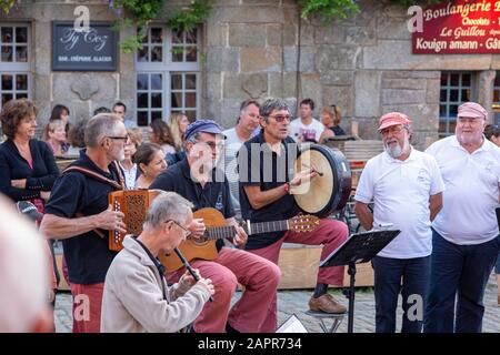 Locronan Dorfplatz; eine Gruppe traditioneller keltischer Sänger versammelt sich am Abend am Dorfplatz und singt traditionelle Volkslieder Stockfoto