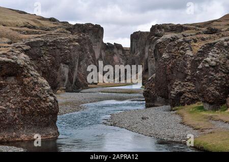 Ein trickender Strom durchschneidet an einem launigen Sommertag den mächtigen, schnürenden Fjadrargljufur Canyon - Südostisland Stockfoto