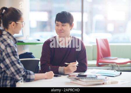 Asiatischer junger Mann sitzt am Tisch und arbeitet mit seinem Kollegen zusammen mit Dokumenten Stockfoto