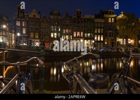 Amsterdam, NIEDERLANDE - 14. Oktober 2019: Blick auf die alten Gebäude in Amsterdam und Fahrräder im Vordergrund bei night Stockfoto