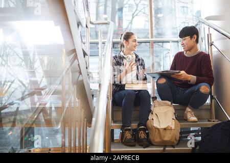 Zwei Studenten sitzen auf einer Treppe mit Laptop und Büchern und diskutieren nach dem Unterricht an der Universität im Team über ihr Projekt Stockfoto
