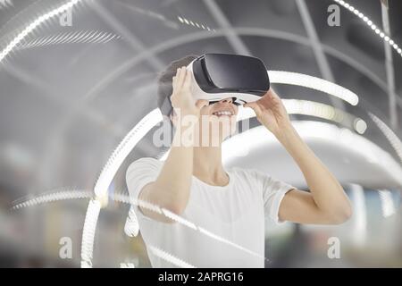 Junge lächelnde Frau, die eine intelligente Brille trägt und das Videospiel genießt Stockfoto